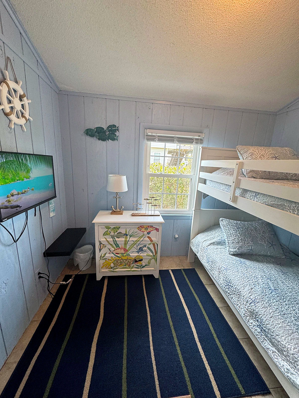 Bunk room with white bunk beds, a ship's wheel and a hand-painted fish dresser