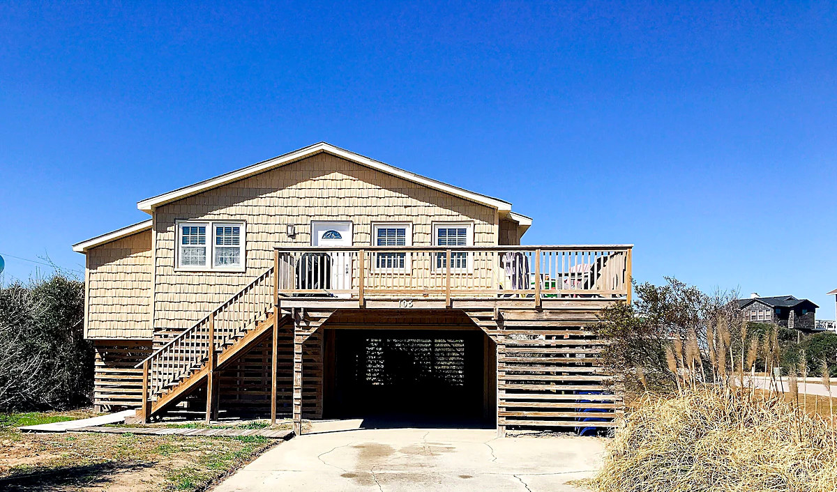 Front of Treasure of the Tides: a raised shingled beach house with a wide deck and stairs